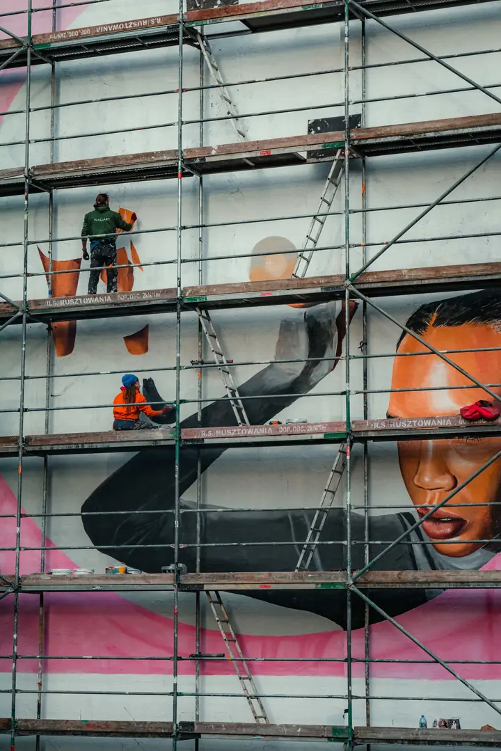 Artistas pintando un mural en una fachada desde un andamio
