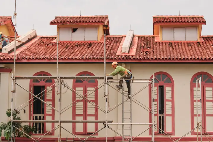 Andamios frente a una fachada con ventanas altas y cubierta de teja
