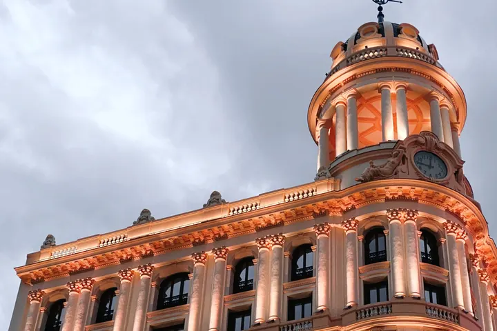 Fachada clásica de un edificio de Madrid con cúpula y reloj, iluminada al atardecer