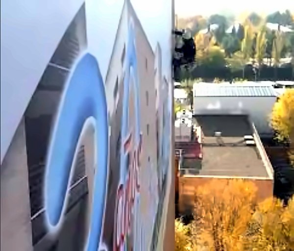 Operario de Grupo Vértigo 2000 instalando con cuerdas una lona publicitaria de gran formato en la fachada de un hospital de Alcalá de Henares