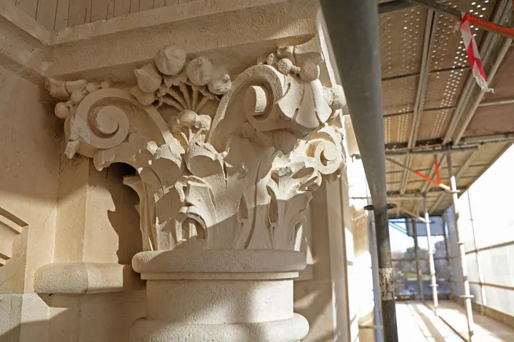 Capitel de piedra restaurado junto al andamio de una fachada