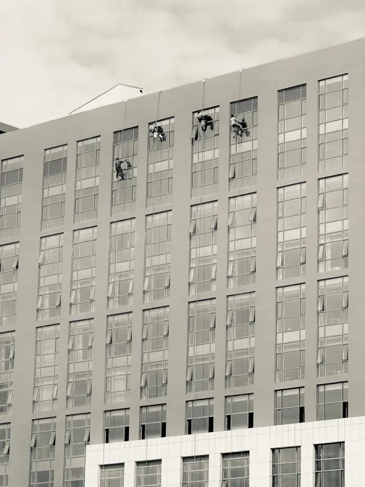 Cuatro operarios limpiando ventanas suspendidos con cuerdas en una fachada